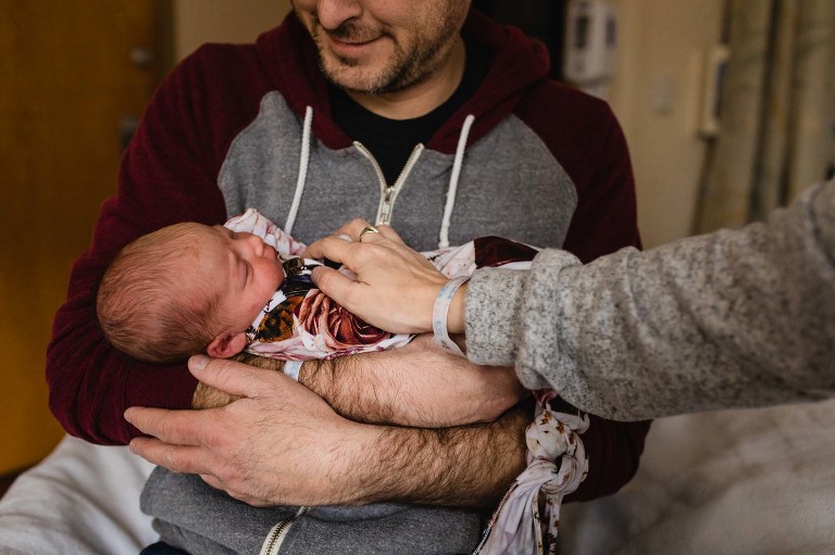 dad smiles, holds his newborn baby for the first time, and mom rests her hand on baby's belly