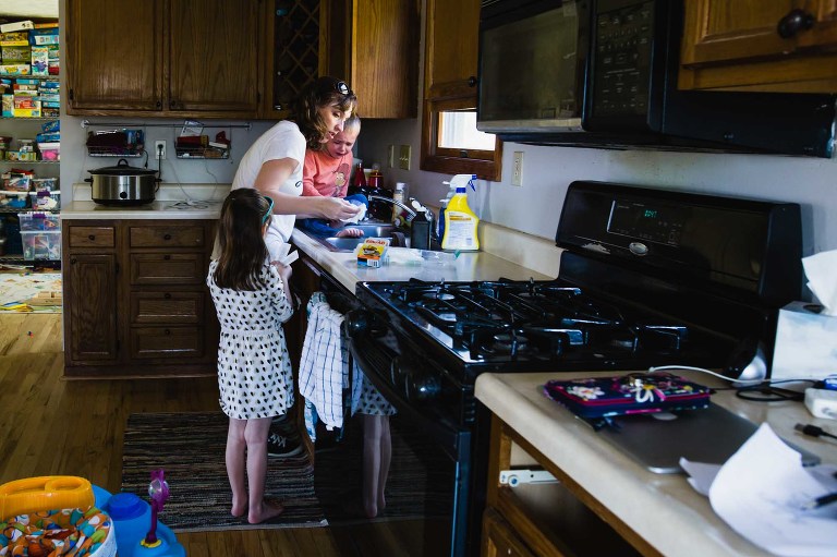mom cleans out injury / boo boo with child in kitchen sink, while little girl hands up bandaids