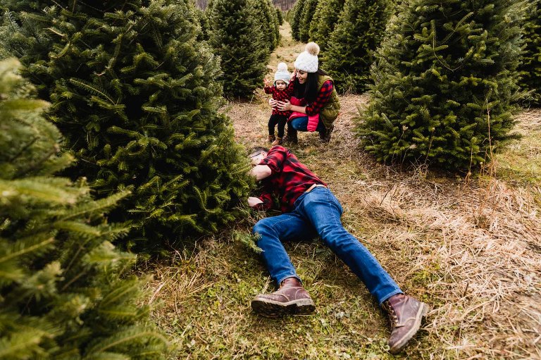 small family cuts down christmas tree together while little girl watches