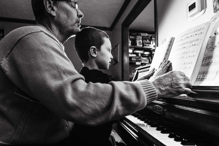 black and white photo of man playing piano with his grandson sitting on his lap