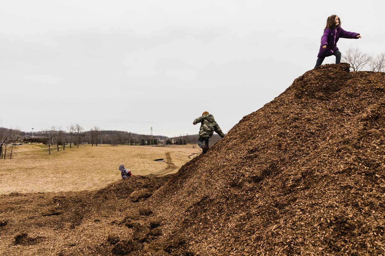kids run up and down a giant mud pile in the country. 