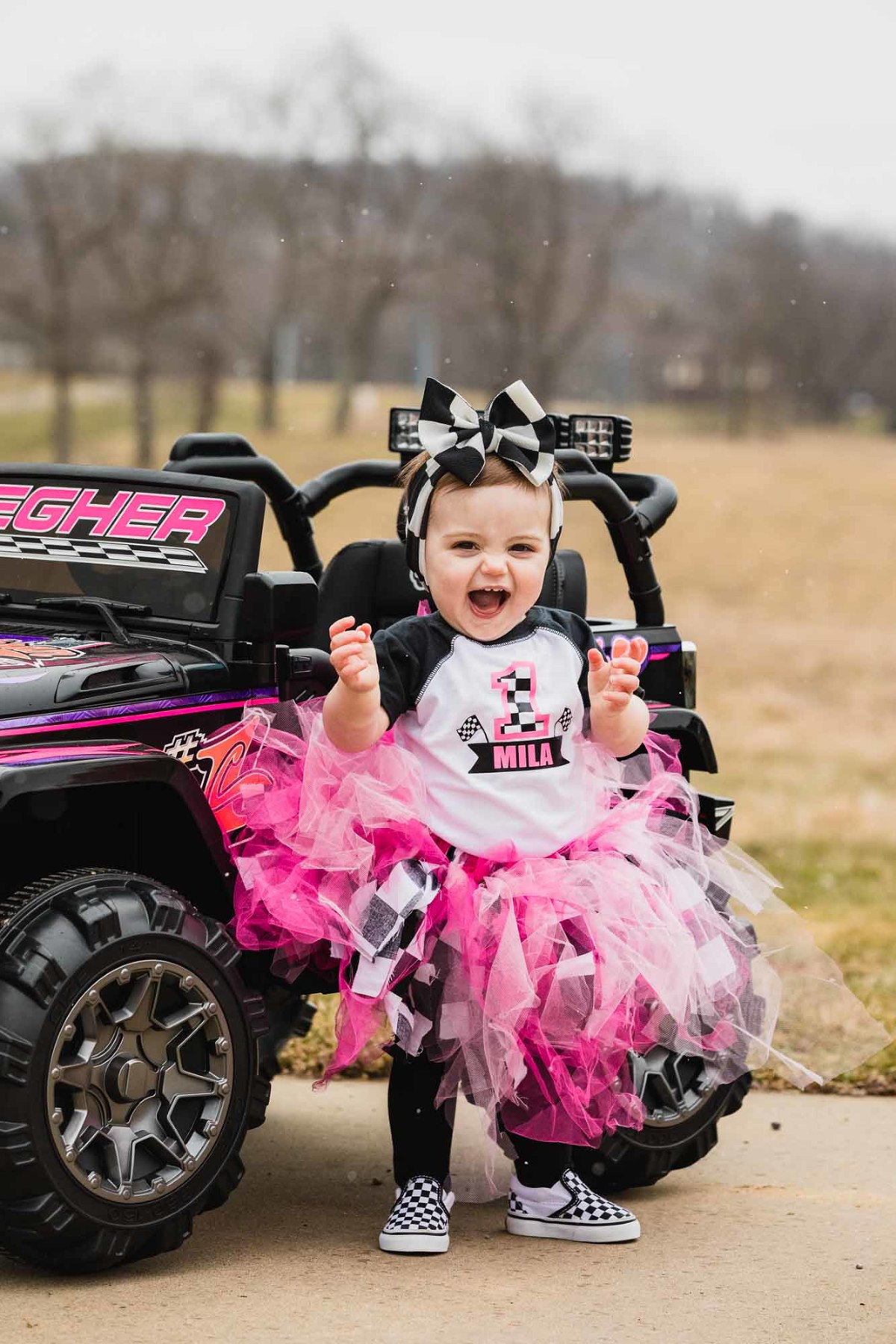 portrait of little girl on her first birthday, wearing a pink tutu and standing in front of a child's size atv.
