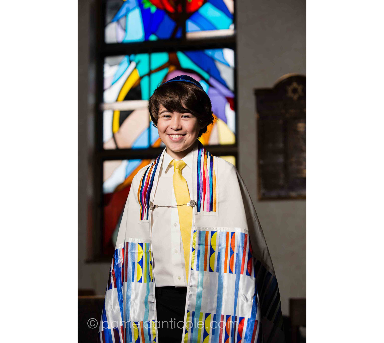 portrait of young boy in bar mitzvah attire, standing in front of stained glass window