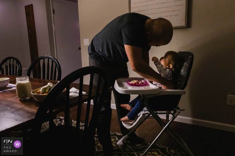 award winning fpja image of little girl in highchair reaching up for her dad who is unbuckling her