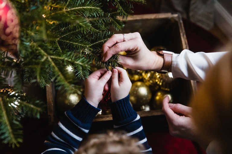 mom and little boy hang ornaments together on the tree; closeup of their hands touching the ornament