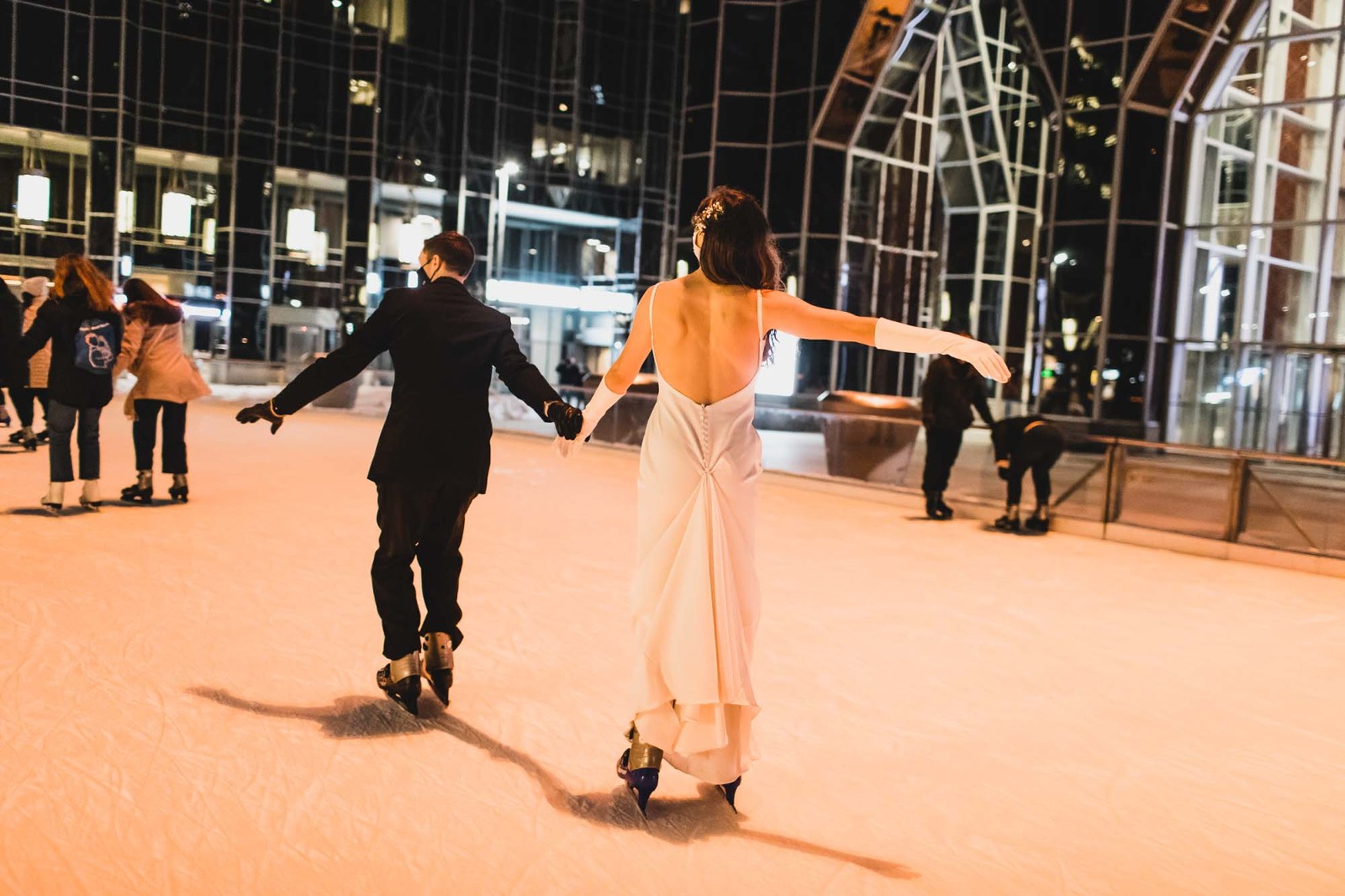 bride and groom ice skating in their wedding dress at night in the city