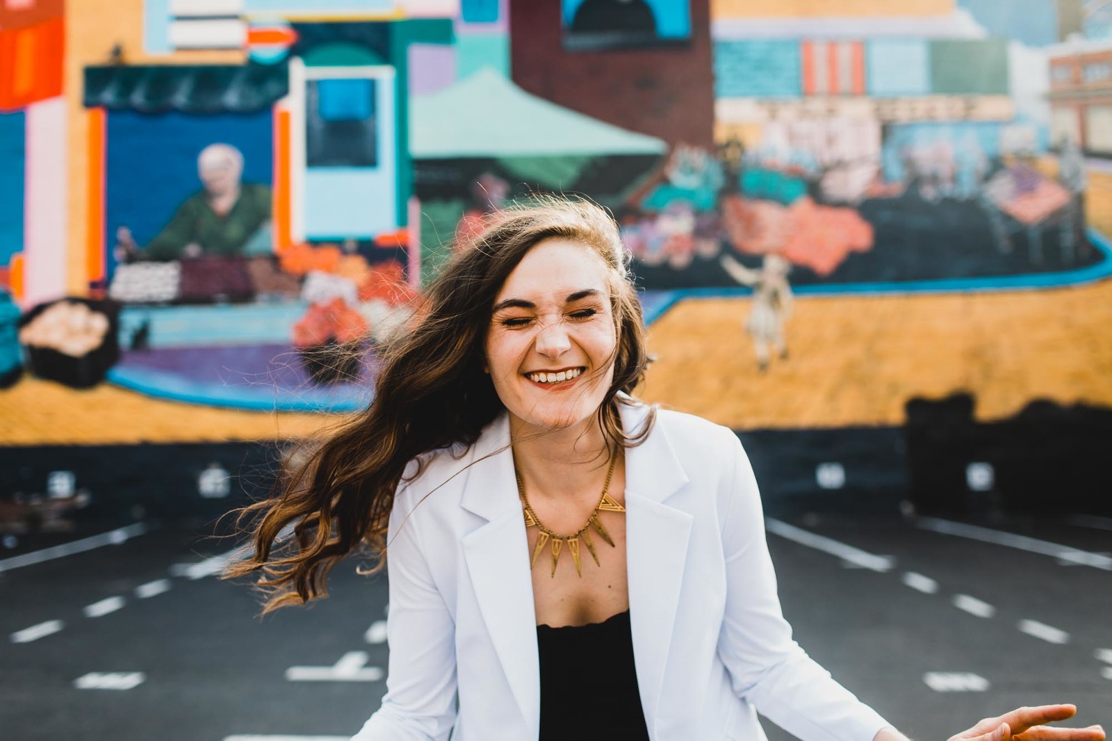 woman laughing with her hair blowing in the wind in front of a colorful mural