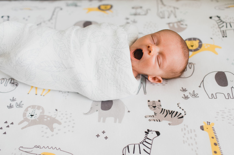newborn baby in her crib, wrapped up and yawning