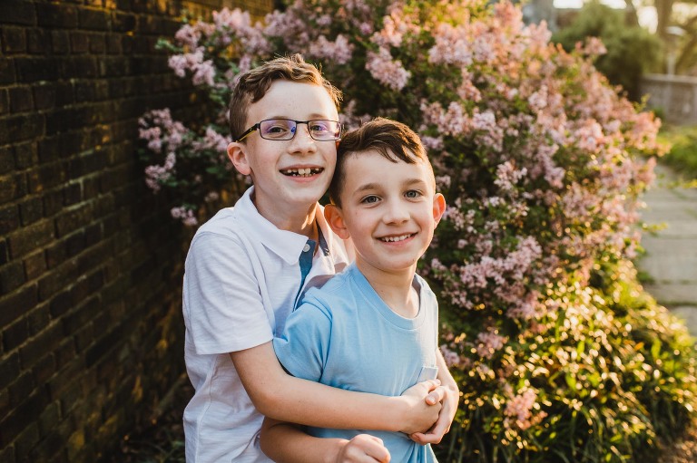 brothers hugging in front of colorful bush in a city park