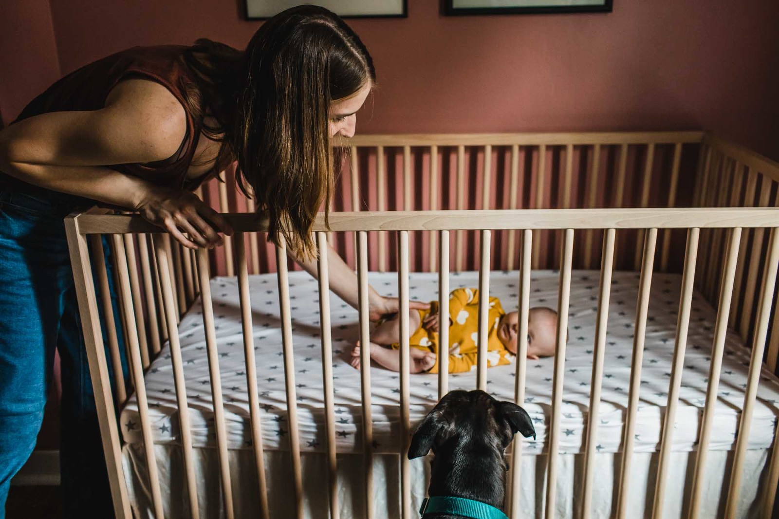 mom and dog looking at baby girl laying in the crib