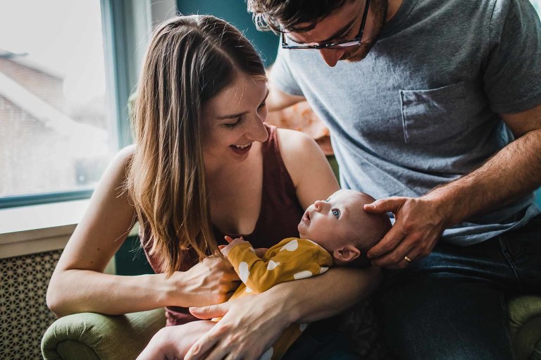 mom and dad holding baby, touching her hands and head gently as she looks up into their eyes
