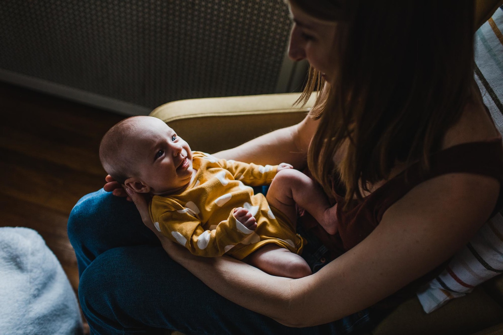 baby girl smiling up at her mom from her lap, lit from moody window light