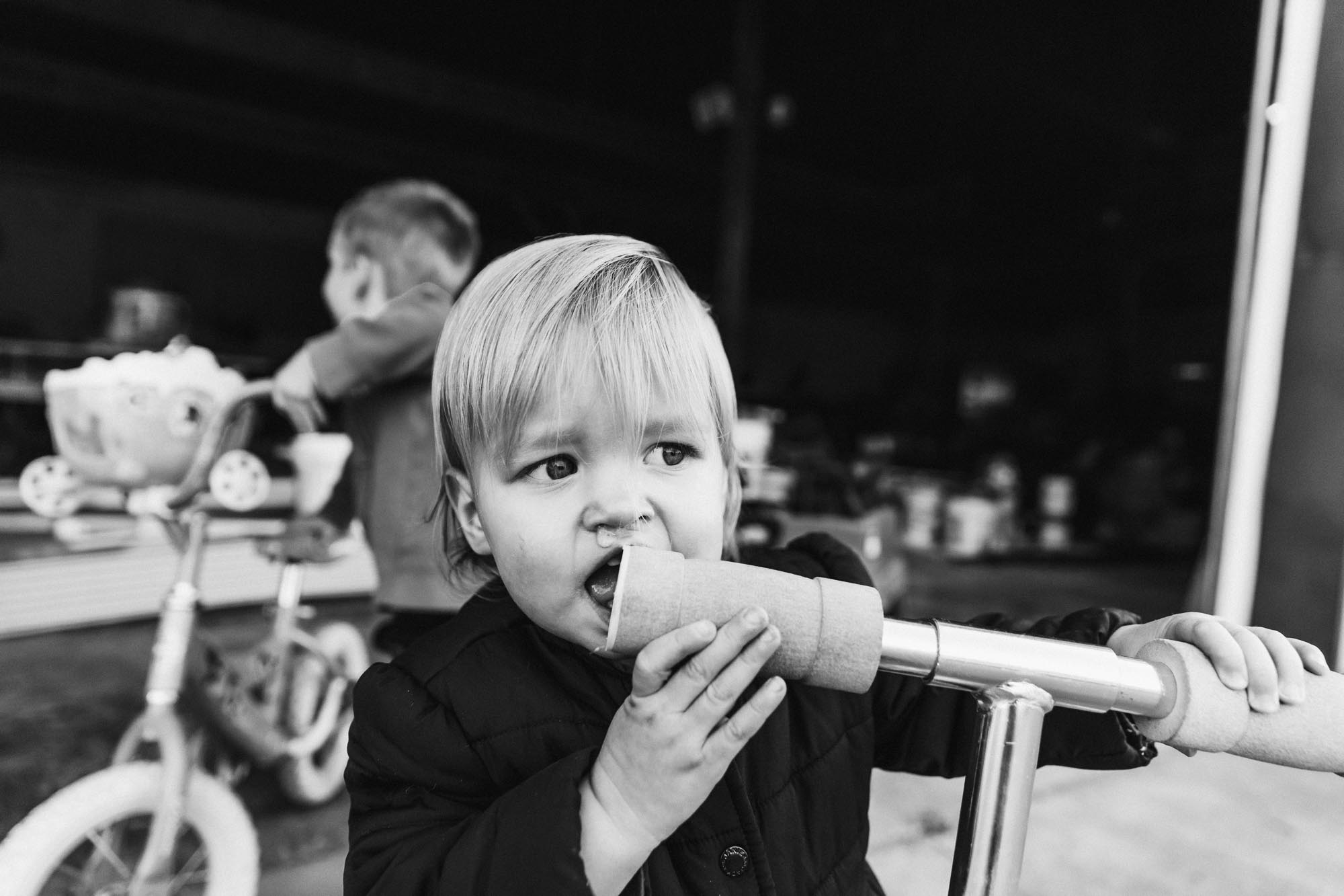 black and white photo of little girl with runny nose chewing on a scooter handle