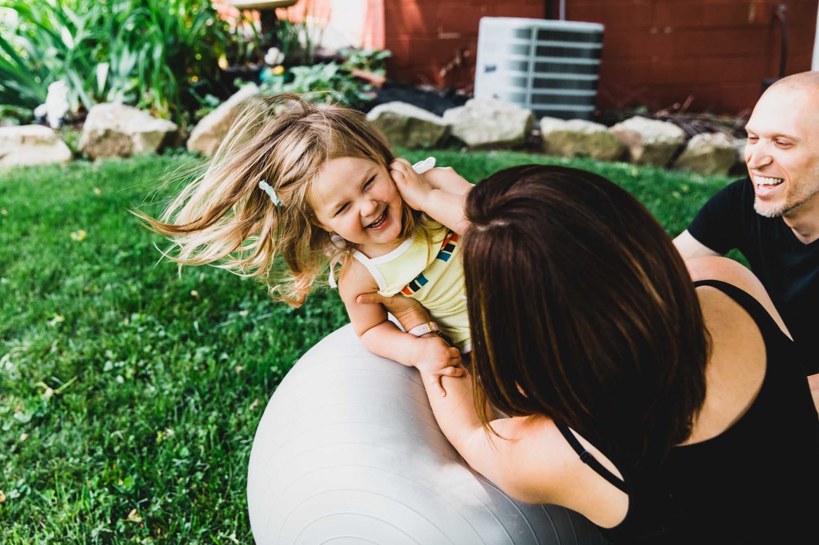 candid moment of little girl bouncing on the ball with her parents, hair flying into the air