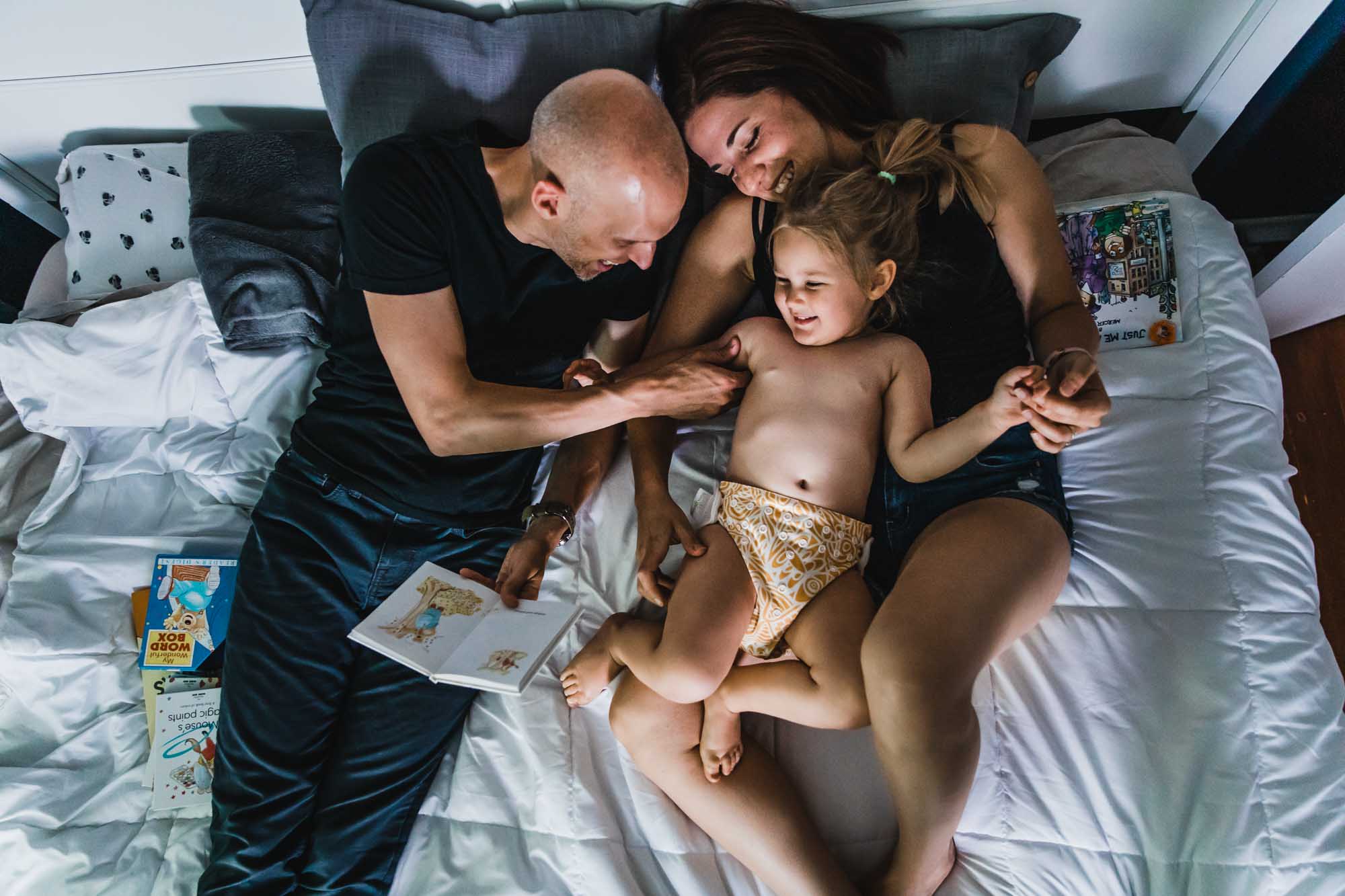 family of 3 reading a book together on the bed, photographed from above