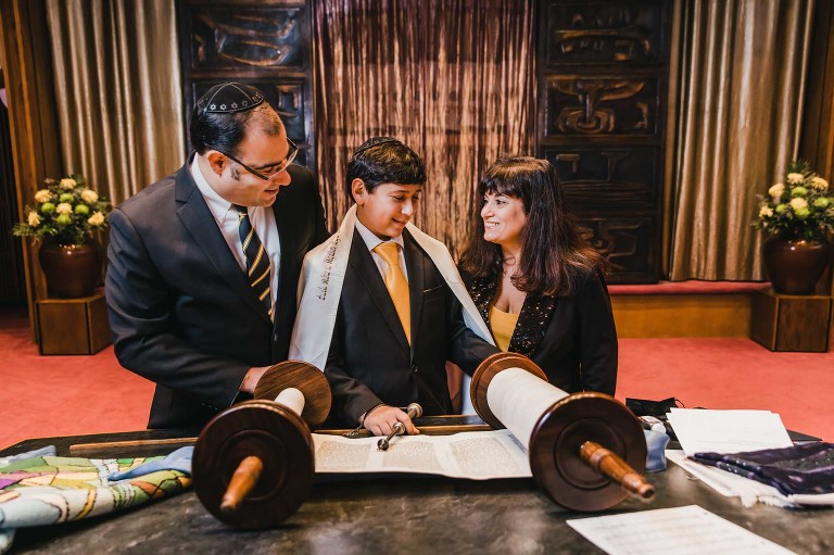 bar mitzvah boy stands at the bimah with his parents, in front of the ark while reading the torah