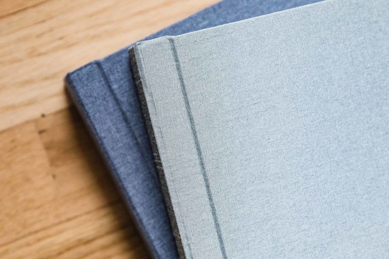 two linen covered albums in neutral blue and gray tones, sitting on a warm hardwood floor background