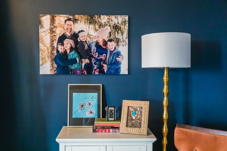 large metal wall print of family photo, hanging above a dresser with pictures and books on it