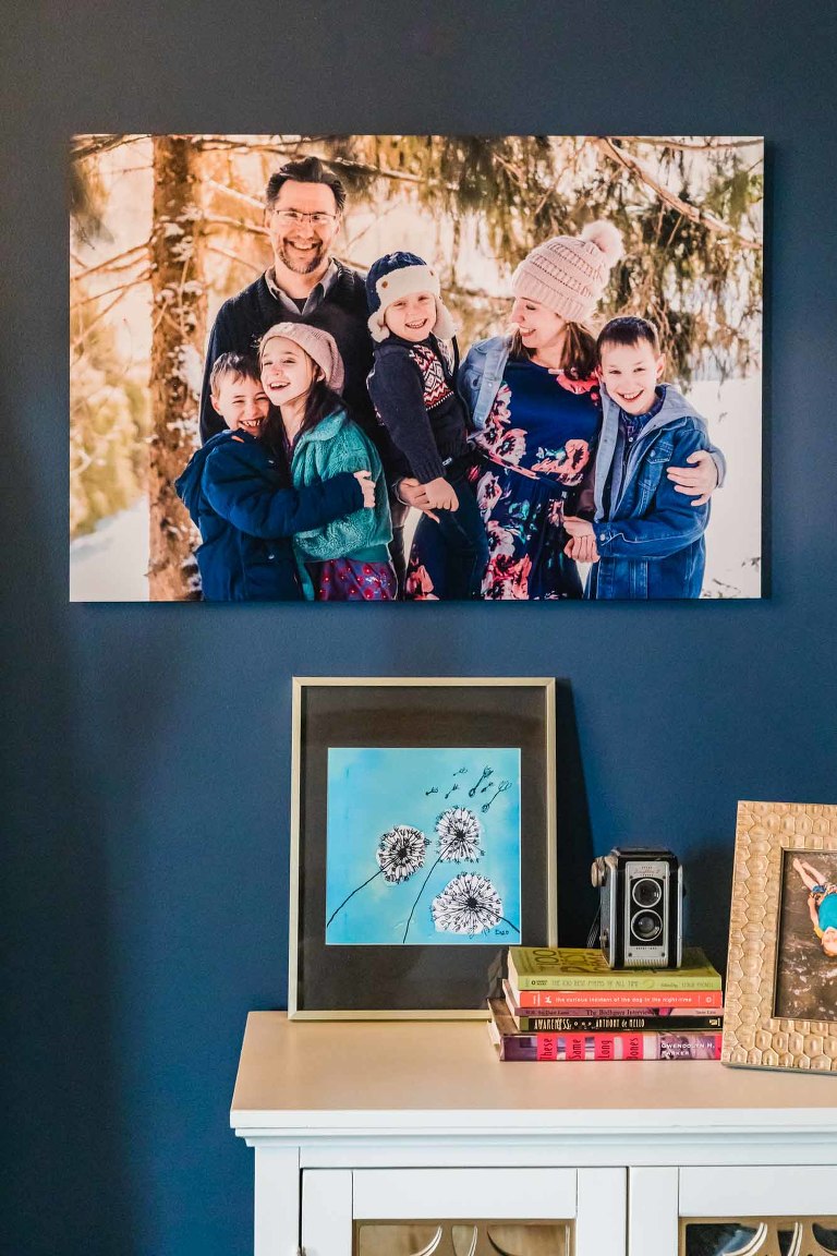 large metal wall print of family photo, hanging above a dresser with pictures and books on it