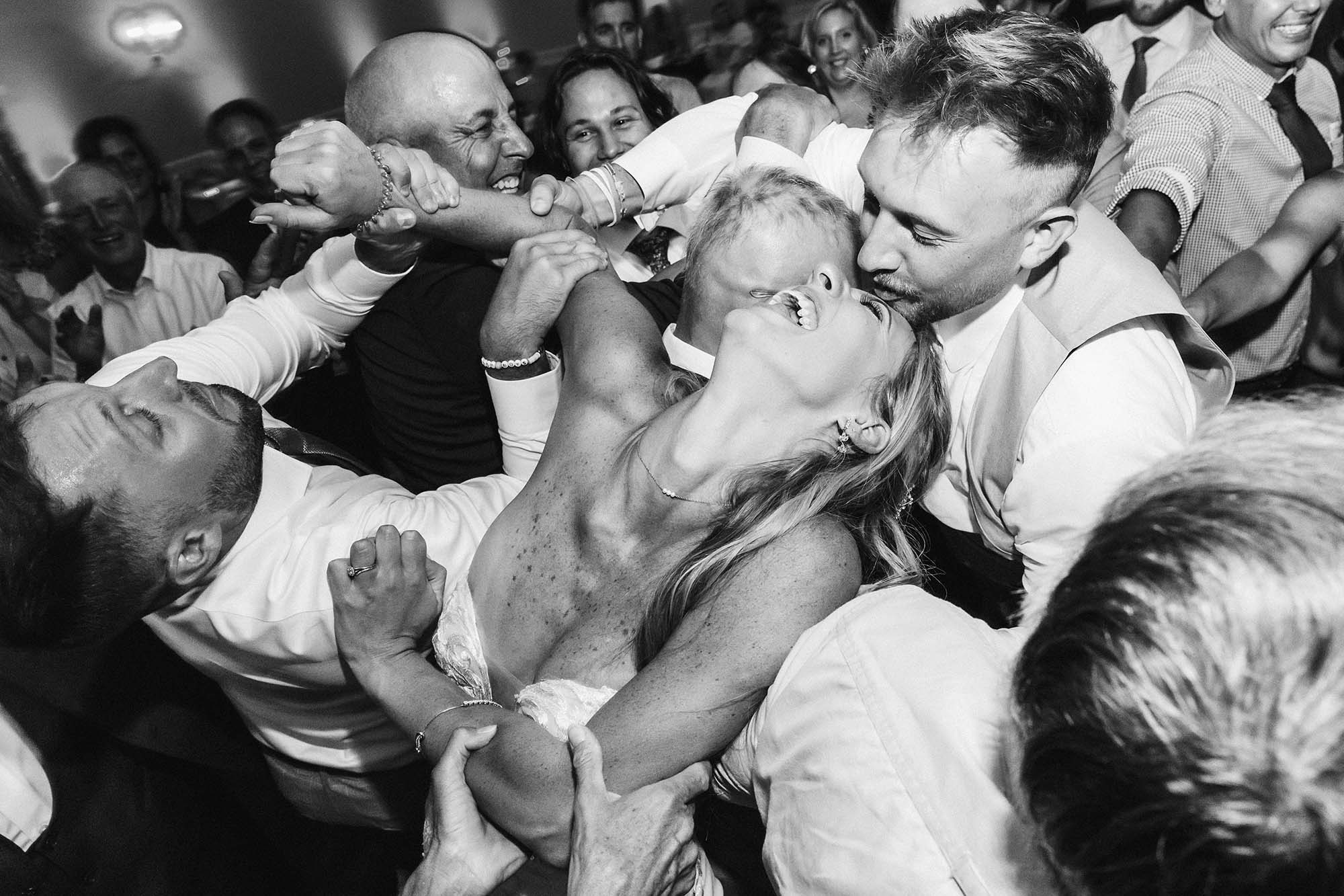 bride being held firmly by dancers on a dance floor during the polka, everybody having fun laughing