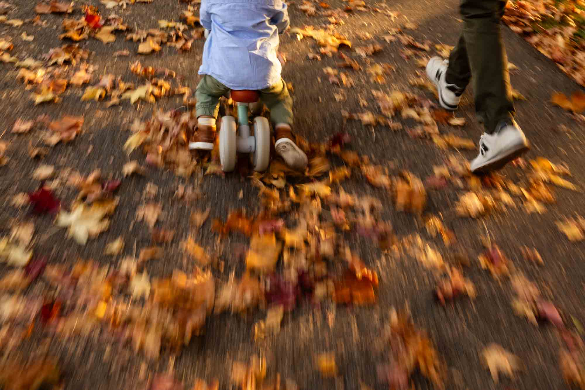 father and son running together along a sidewalk filled with fall foliage leaves, with motion blur