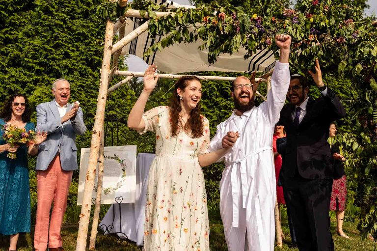 bride and groom celebrate after breaking the glass under the chuppah at their wedding ceremony, outside at aspinwall riverfront in pittsburgh pa