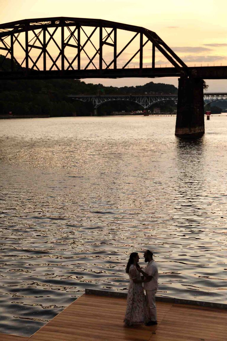 bride and groom snuggle together in front of the allegheny river with pittsburgh bridge in the background