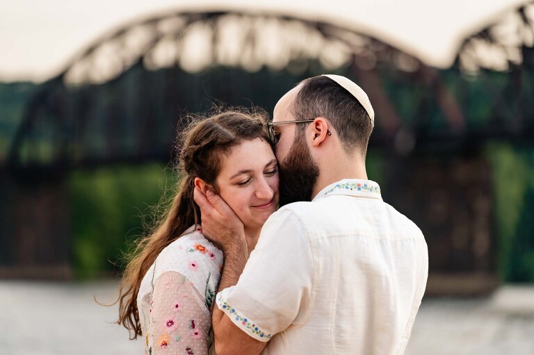 couple snuggles in front of a bridge over the allegheny river