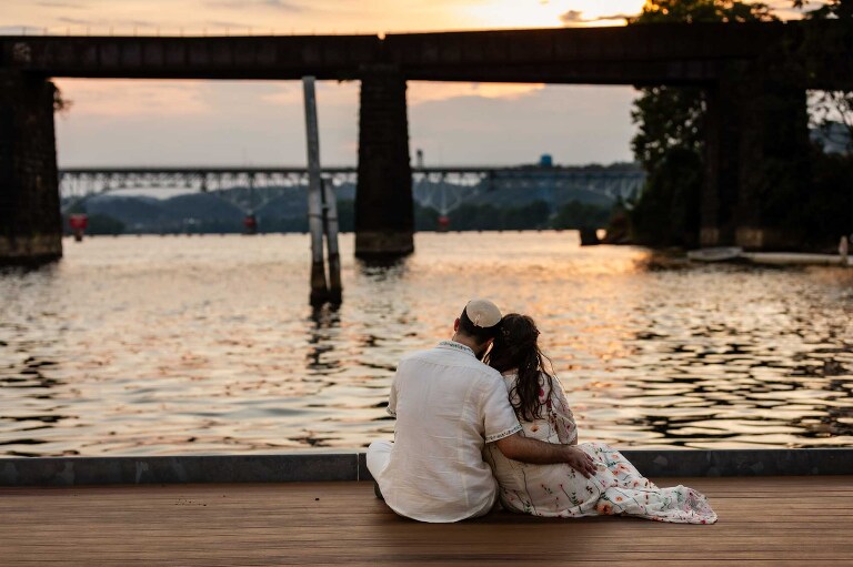 sunset photo of a couple sitting on the dock in front of the allegheny river, at the gem on the allegheny wedding venue in pittsburgh pa