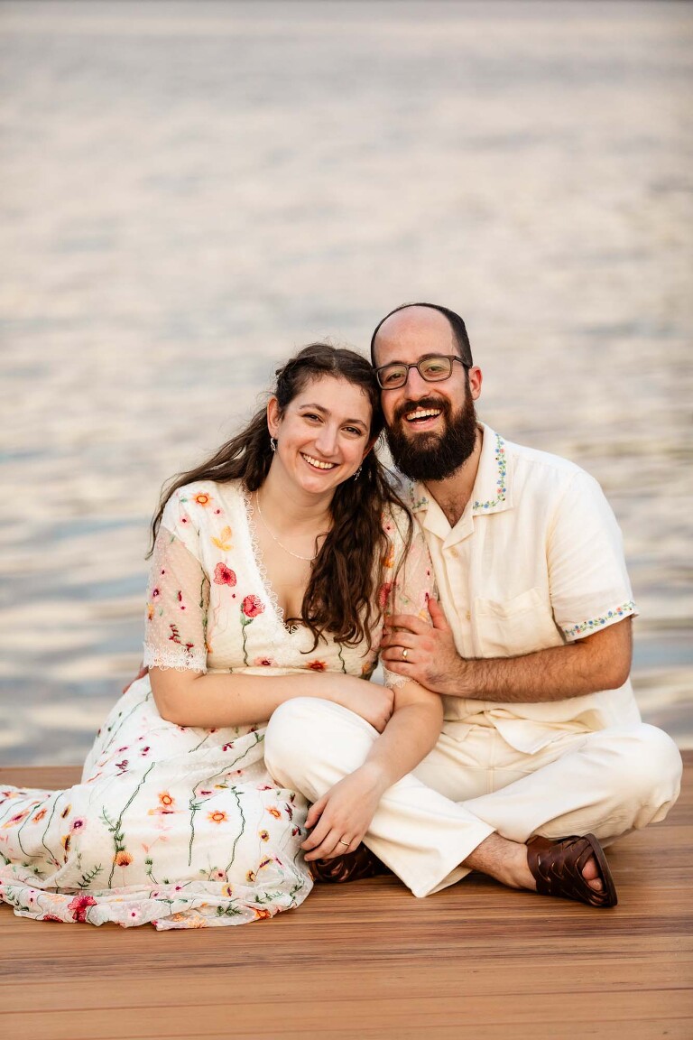 bride and groom sitting on a dock with water in the background