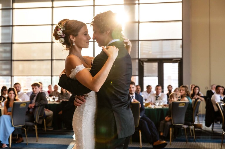 bride and groom dance in front of their guests and the pittsburgh skyline at the duquesne power center ballroom