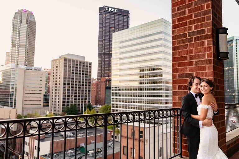 bride and groom snuggling together in front of downtown pittsburgh, from the balcony of the dougherty ballroom at duquesne power center