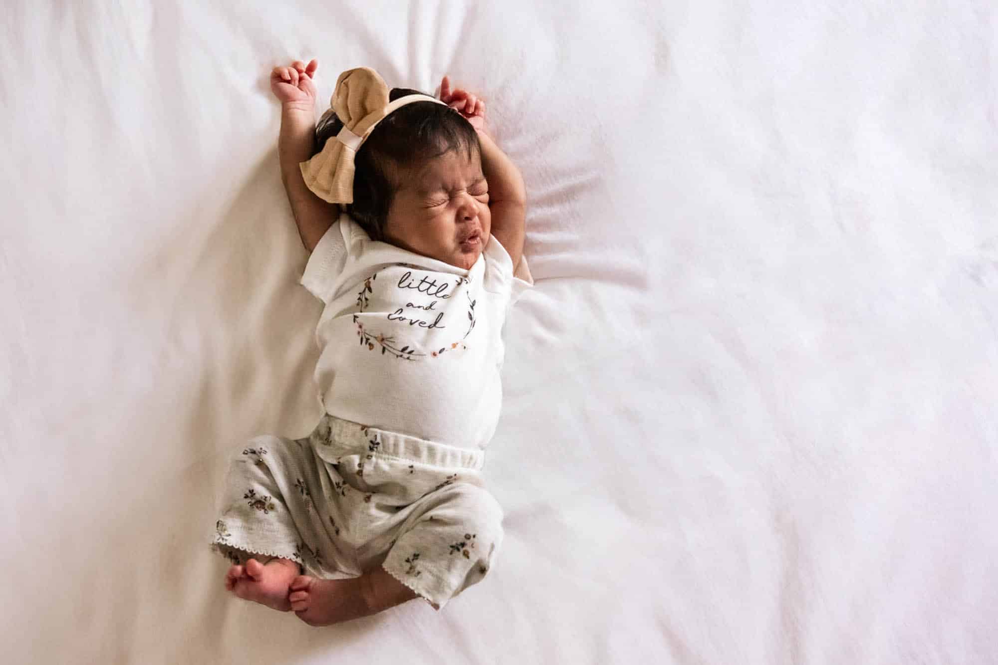 baby girl lying on bed stretches out with grumpy yawning face, taken by a newborn photographer in pittsburgh, Pamela anticole