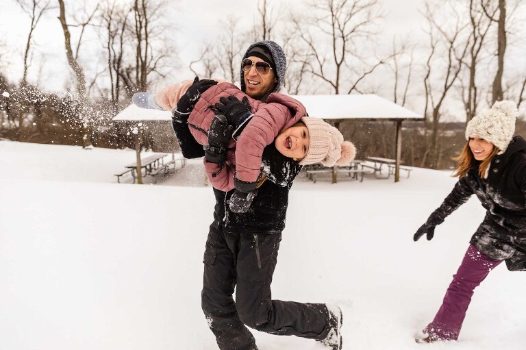 dad carries daughter in the snow with mom chasing them, everyone laughing, at this unique photoshoot location in pittsburgh: boyce park!