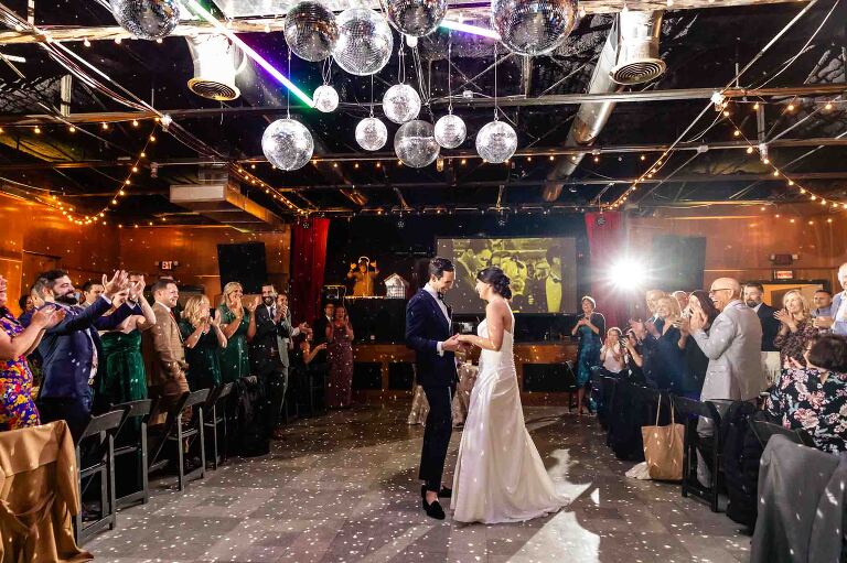 one of the most unique wedding venues in pittsburgh, spirit offers a funky eclectic vibe easily customizable to your wedding style. this photo features a bride and groom dancing in the grand hall surrounded by wedding guests under an array of disco balls