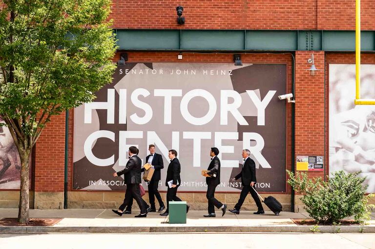 groomsmen walk down the street in front of the heinz history center for the wedding photos