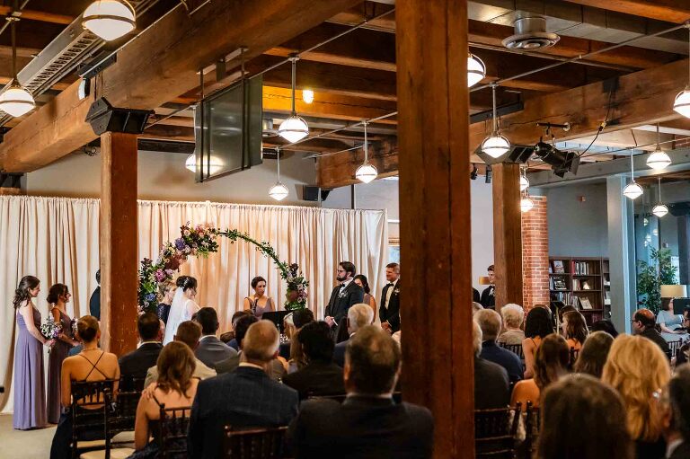 wedding ceremony in the library in front of a purple arch, as part of a heinz history center wedding photographed by pamela anticole