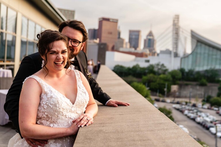 bride and groom laughing on the balcony, overlooking pittsburgh, as part of their heinz history center wedding day.
