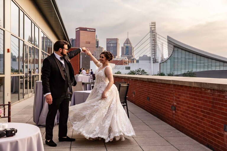 bride and groom dance together on the balcony, as the sun set over the city of pittsburgh in the background, at their heinz history center wedding. pictures by documentary wedding photographer pamela anticole
