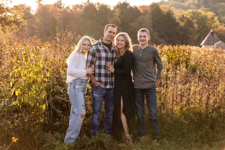 family with older kids standing in front of tall grasses in autumn at sunset