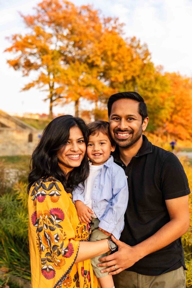 young indian family standing in front of yellow and red fall foliage in pittsburgh's schenley park