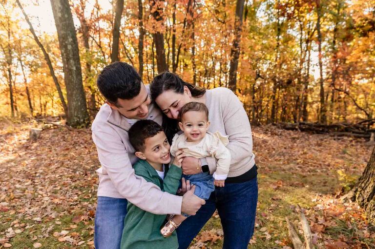 young family playing together in the woods surrounded by fall foliage