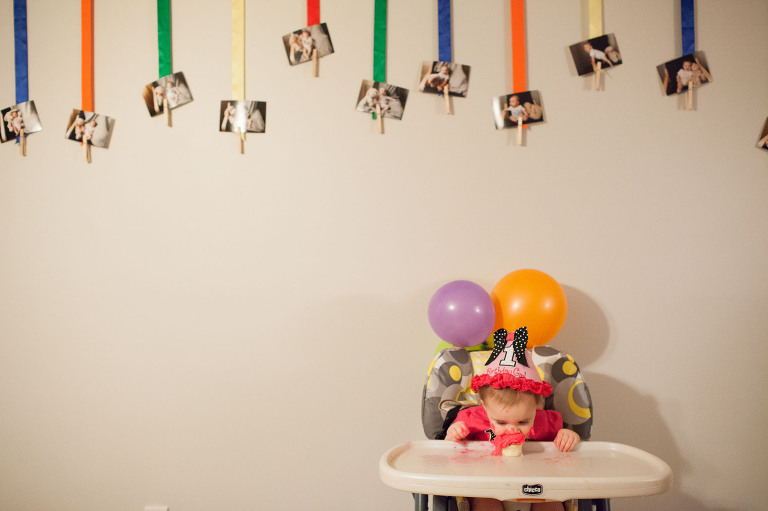 smash cake in high chair at home, in front of photos
