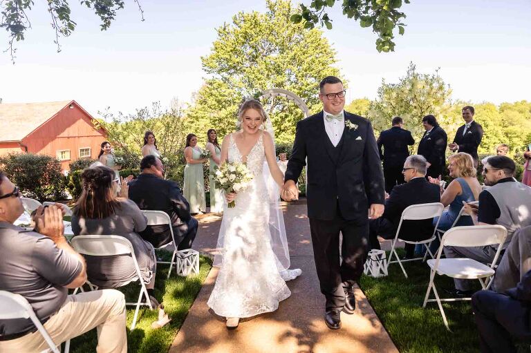 bride and groom just married outside walking down the aisle between their guests at pinehall at eisler farms