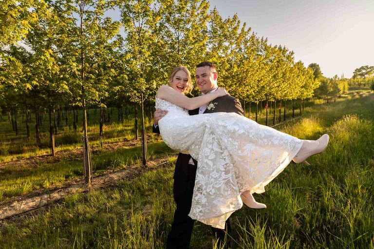 groom carrying bride through a field at pinehall at eisler farms after their ceremony