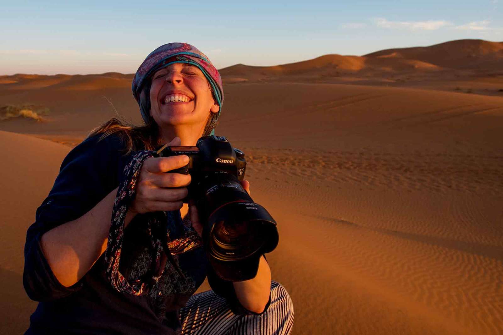 candid picture of woman laughing in the desert, holding a canon dslr camera